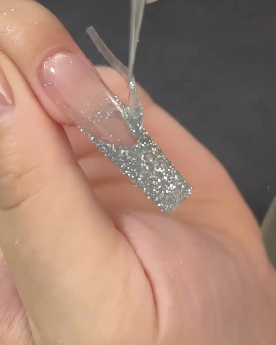 Tweezers pulling a French tip sticker guide off a long nail, revealing a sharp line.