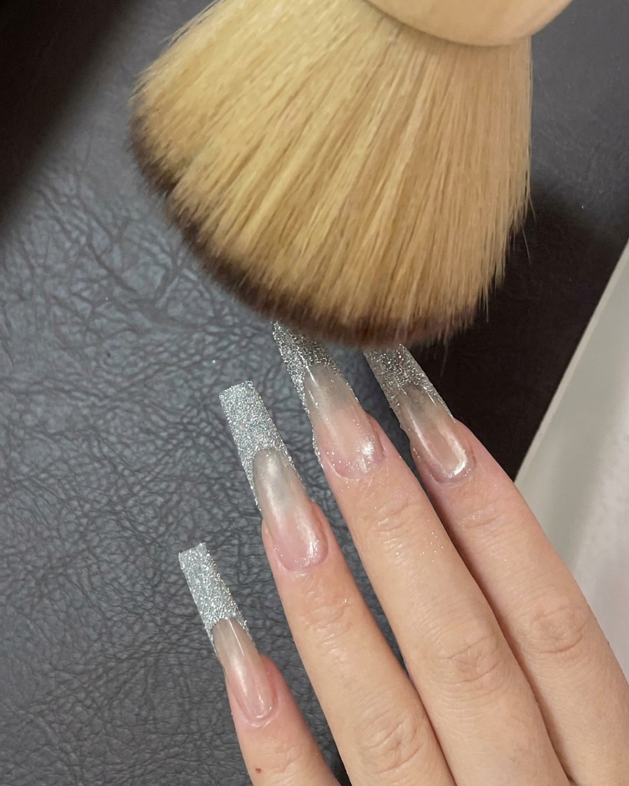 A soft, fluffy brush sweeping over nails to remove final traces of loose glitter powder.