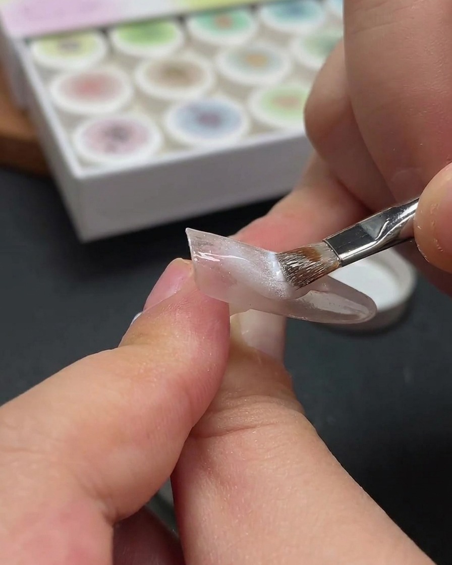 A close-up showing a magnetic wand hovering over a fingernail to shift the metallic particles in the wet white cat-eye gel.