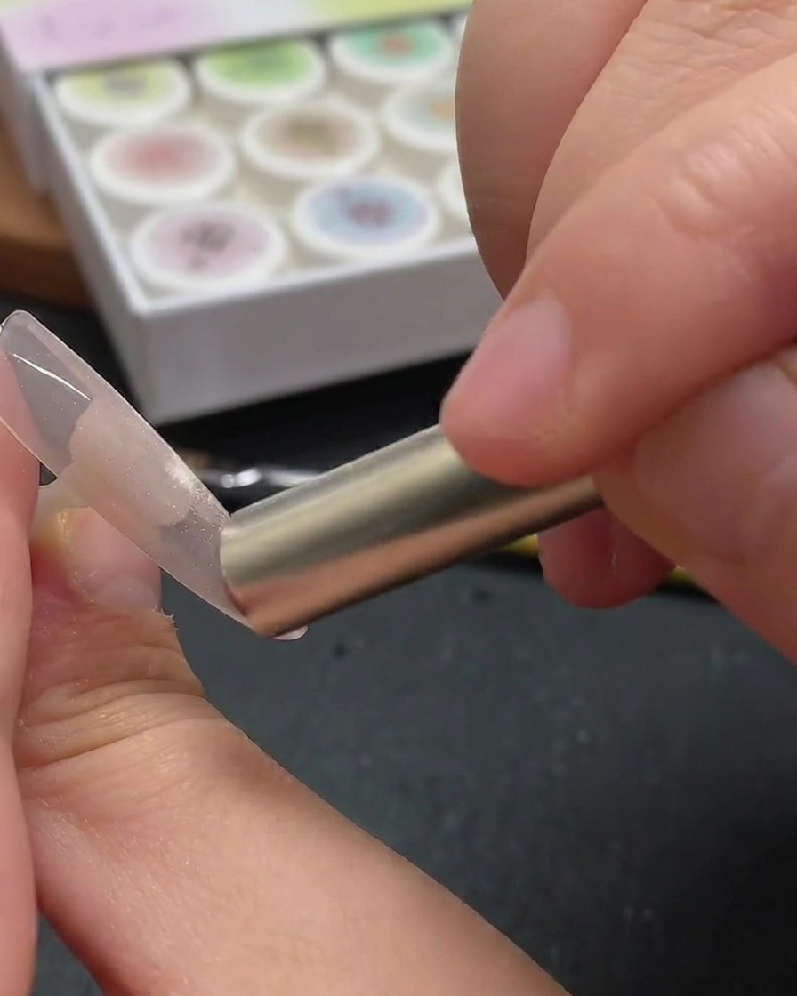 A fingernail illuminated by the purple light of a UV/LED curing lamp, setting the cat-eye gel design.
