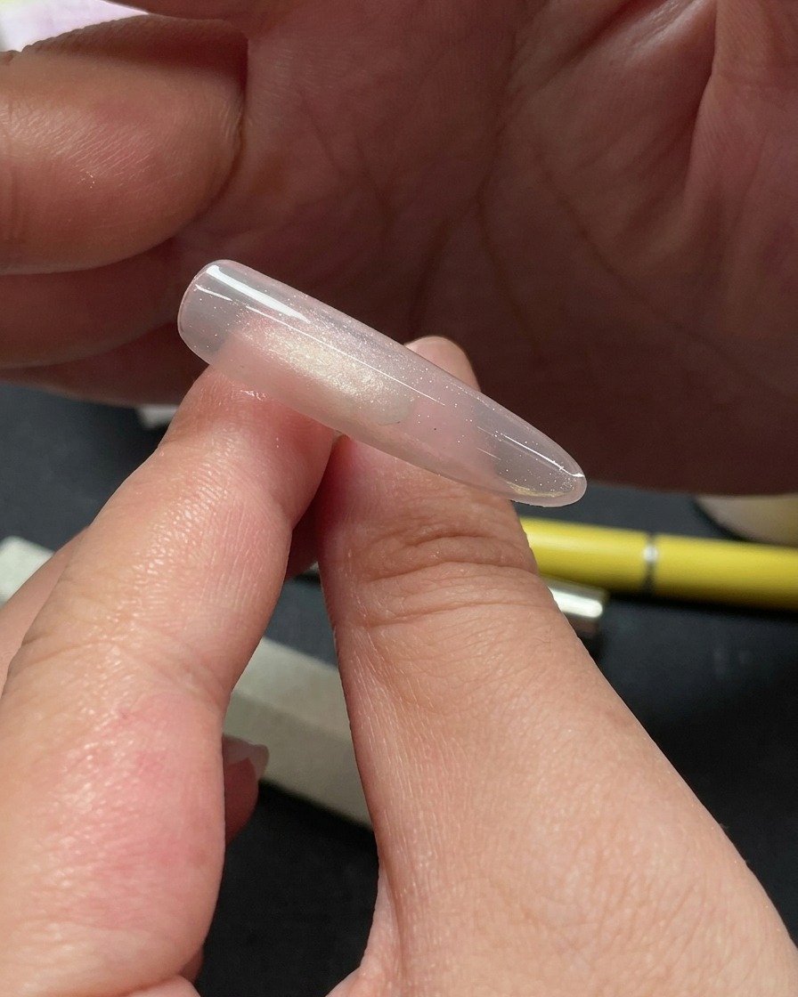 Close-up of a hand using a tool to place small, shimmering glitter pieces on the top section of a cat-eye gel nail.