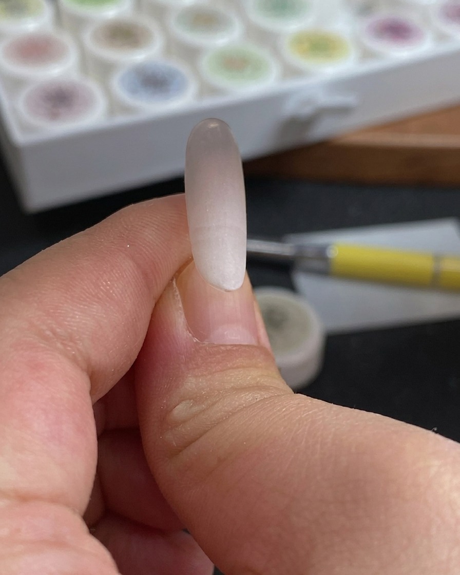 A close-up of a sponge being dabbed onto a nail tip to create a soft rose-red and white color gradient.
