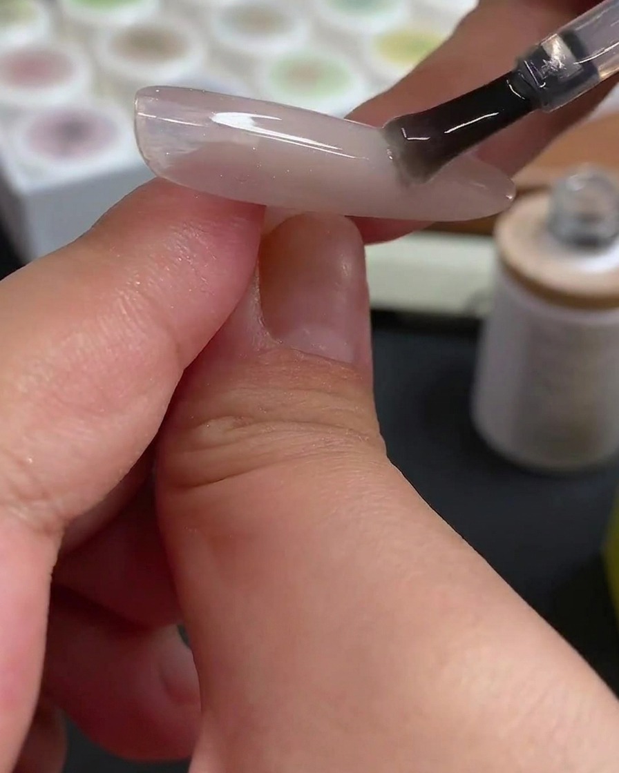 A dotting tool applying precise rose-red gel dots onto a prepped nail surface.
