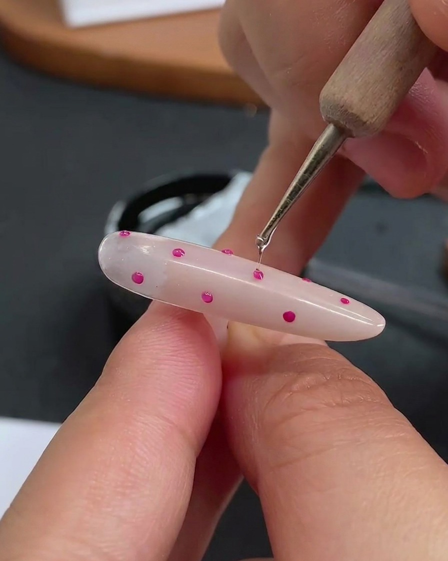 A dotting tool applying a small, clear drop of hard gel over each individual polka dot.