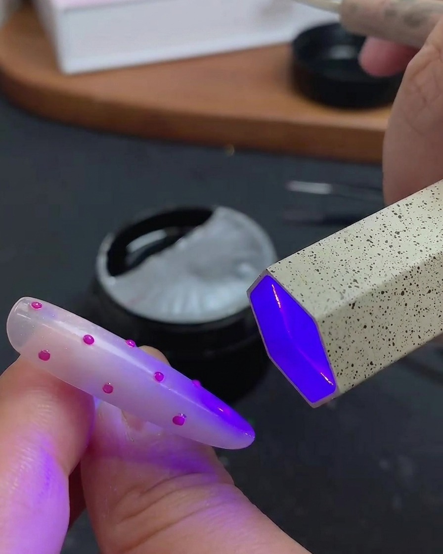 A brush applying a clear, glossy top coat over the 3D polka dot nail art.