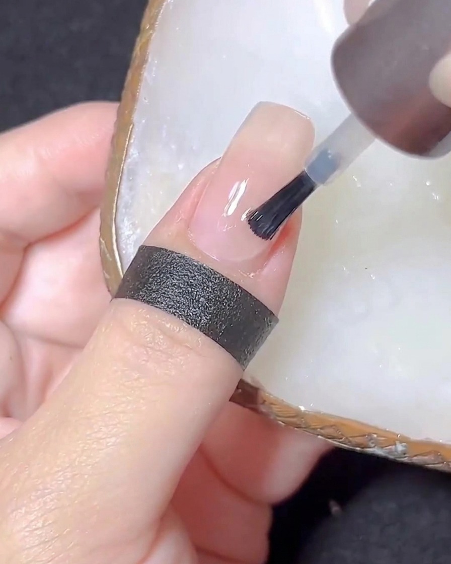 A nail brush applying a clear top coat to a nude-colored nail.
