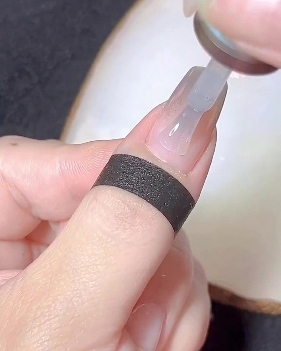 A nail brush applying a thin layer of clear base gel over a chrome-dusted nail.