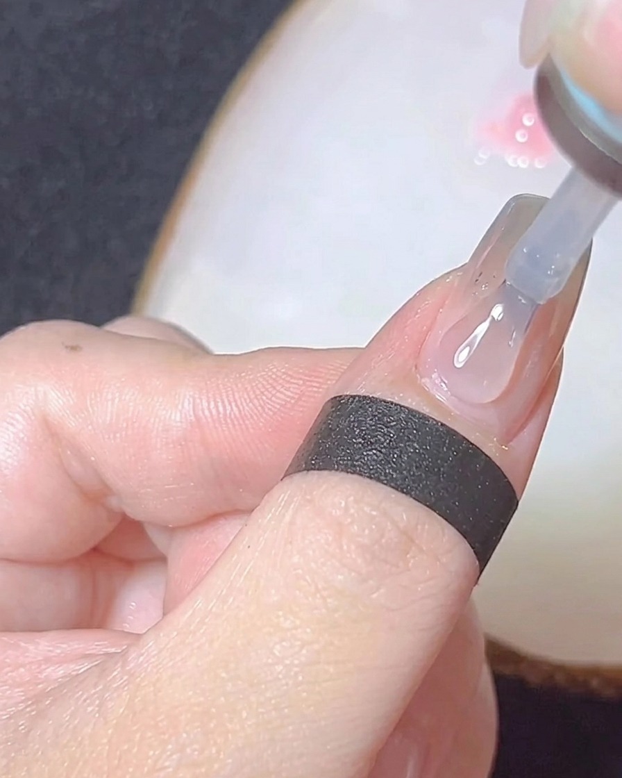 A close-up of a brush applying a glossy clear top coat over a chrome-finished nail.
