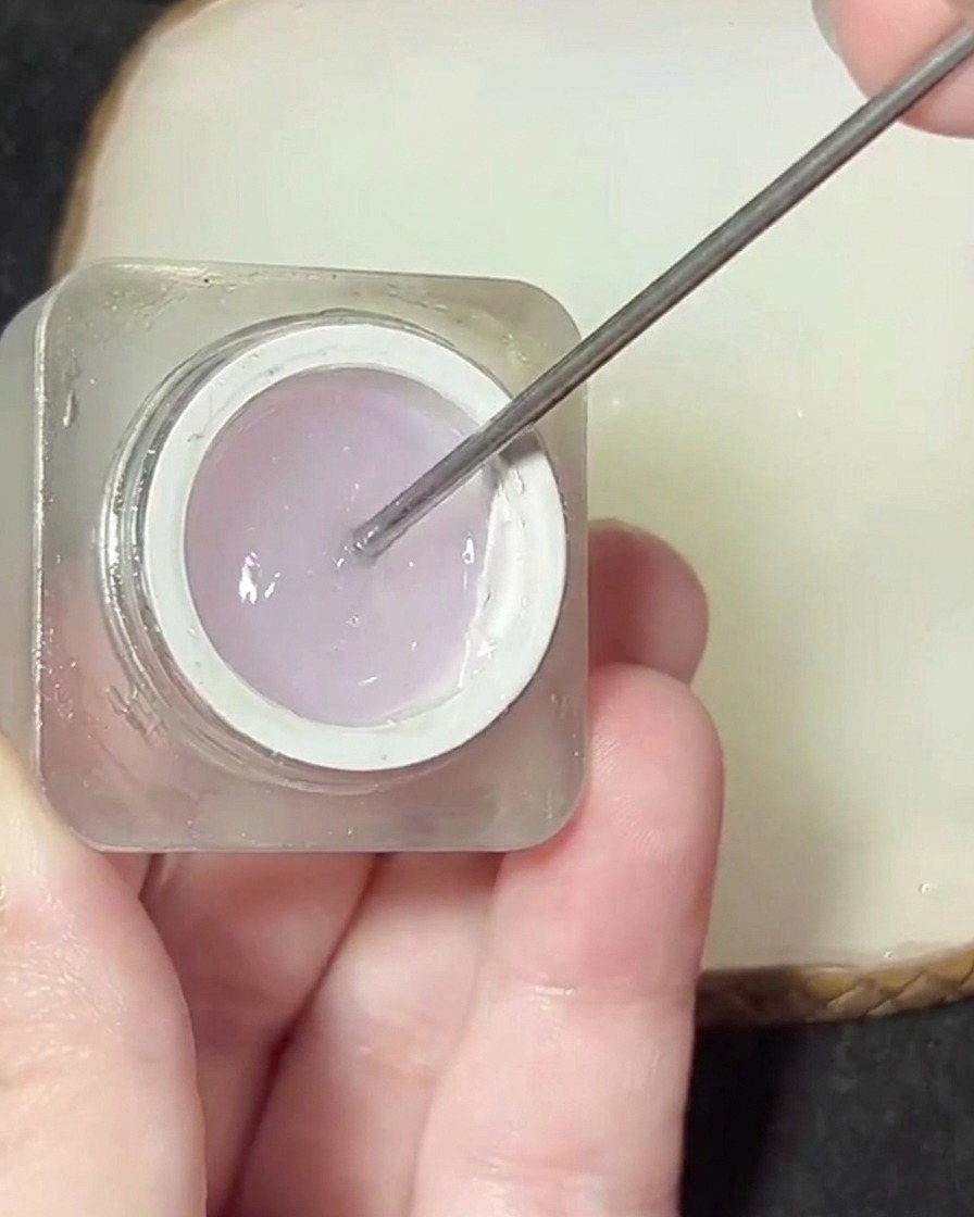 A metal spatula lifting a clear, thick gel product out of a small jar.
