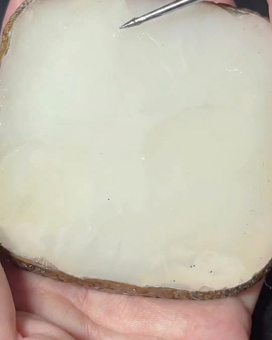 A metal spatula blending a pink pigment into a clear gel base on a stone palette.