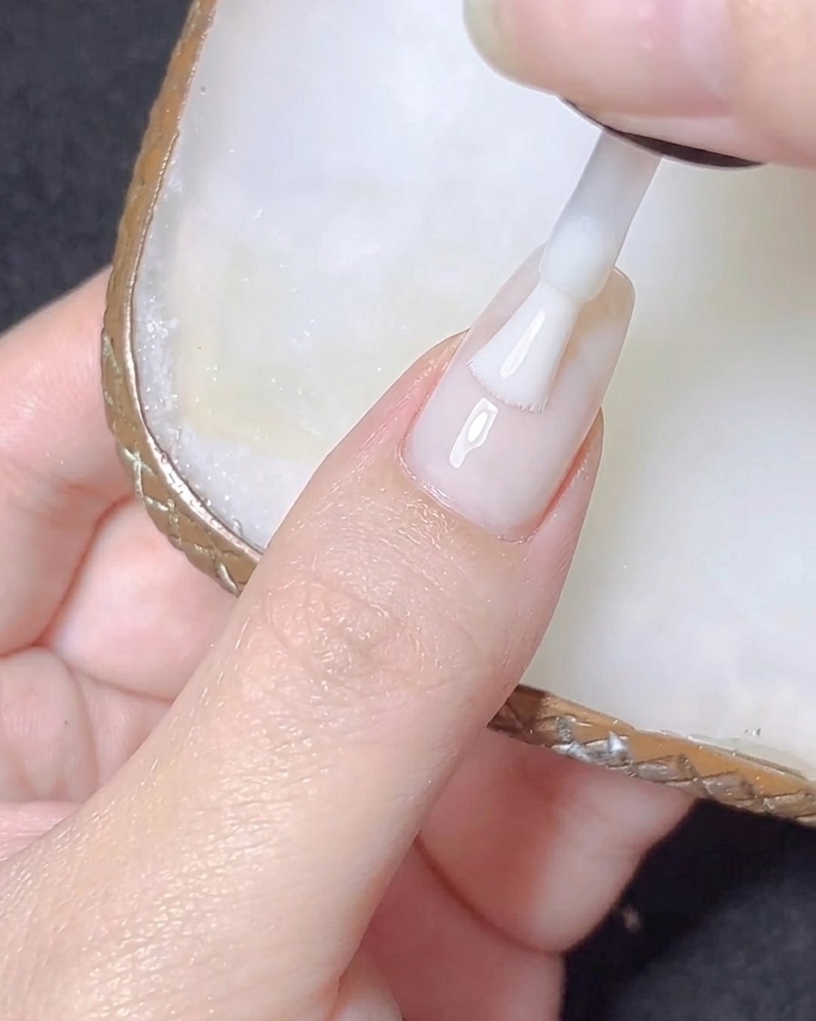 A clear almond-shaped nail extension tip being pressed onto a natural nail plate.