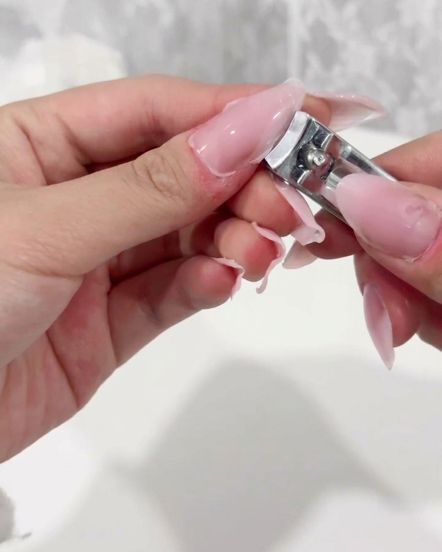 Nail clippers trimming the free edge of a clear plastic nail extension tip.