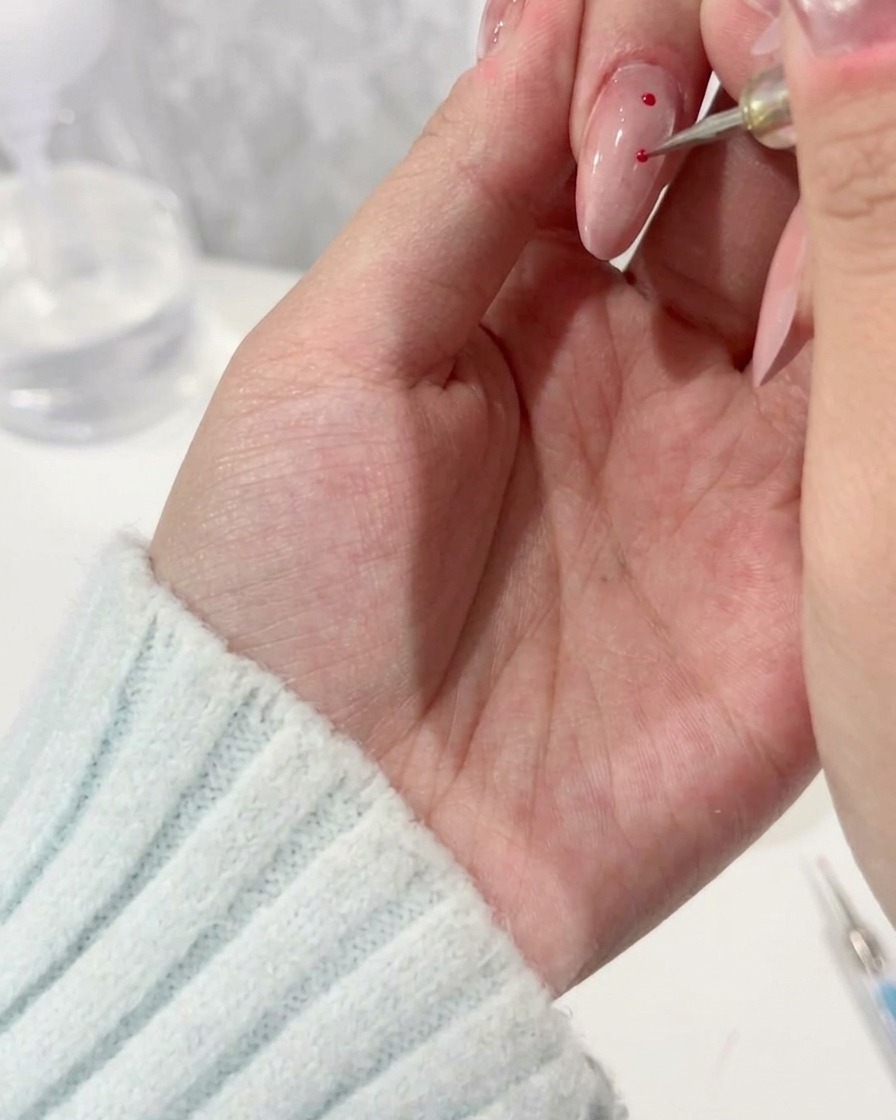 A dotting tool applying precise magenta polka dots onto a light-colored nail base.