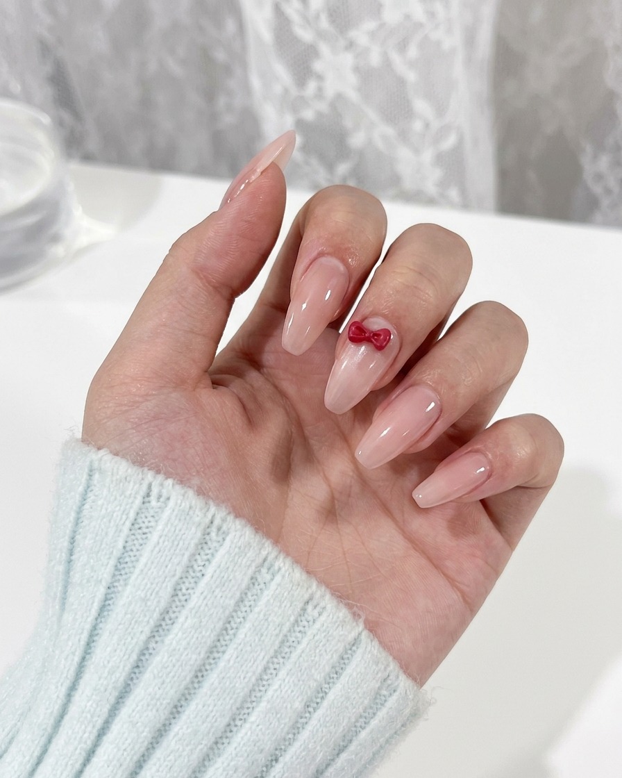 A detail brush painting small red eye shapes on a fingernail beneath a bow charm