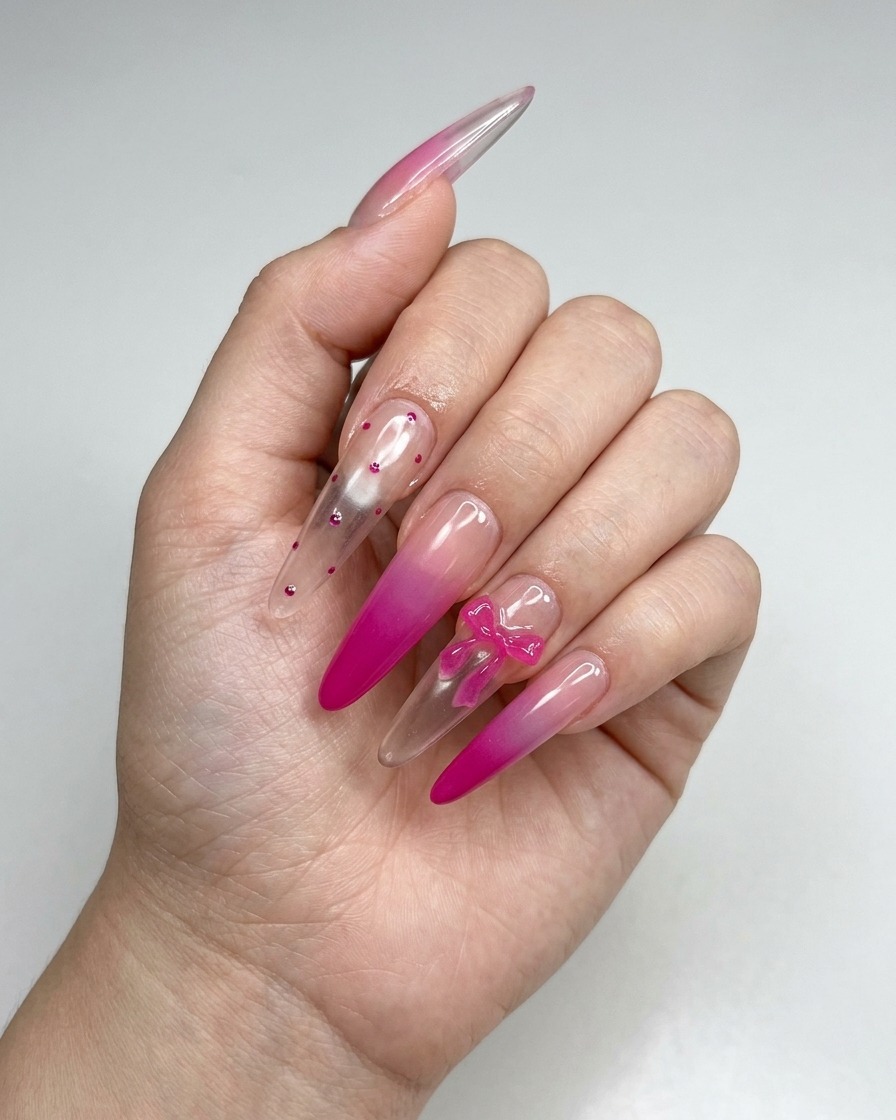 A pair of tweezers placing a small 3D pink bow charm onto the surface of a manicured nail.