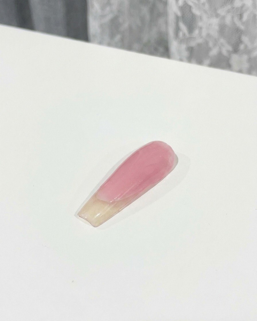 A brush applying a layer of top coat over a 3D pink bow charm fixed onto a nail.