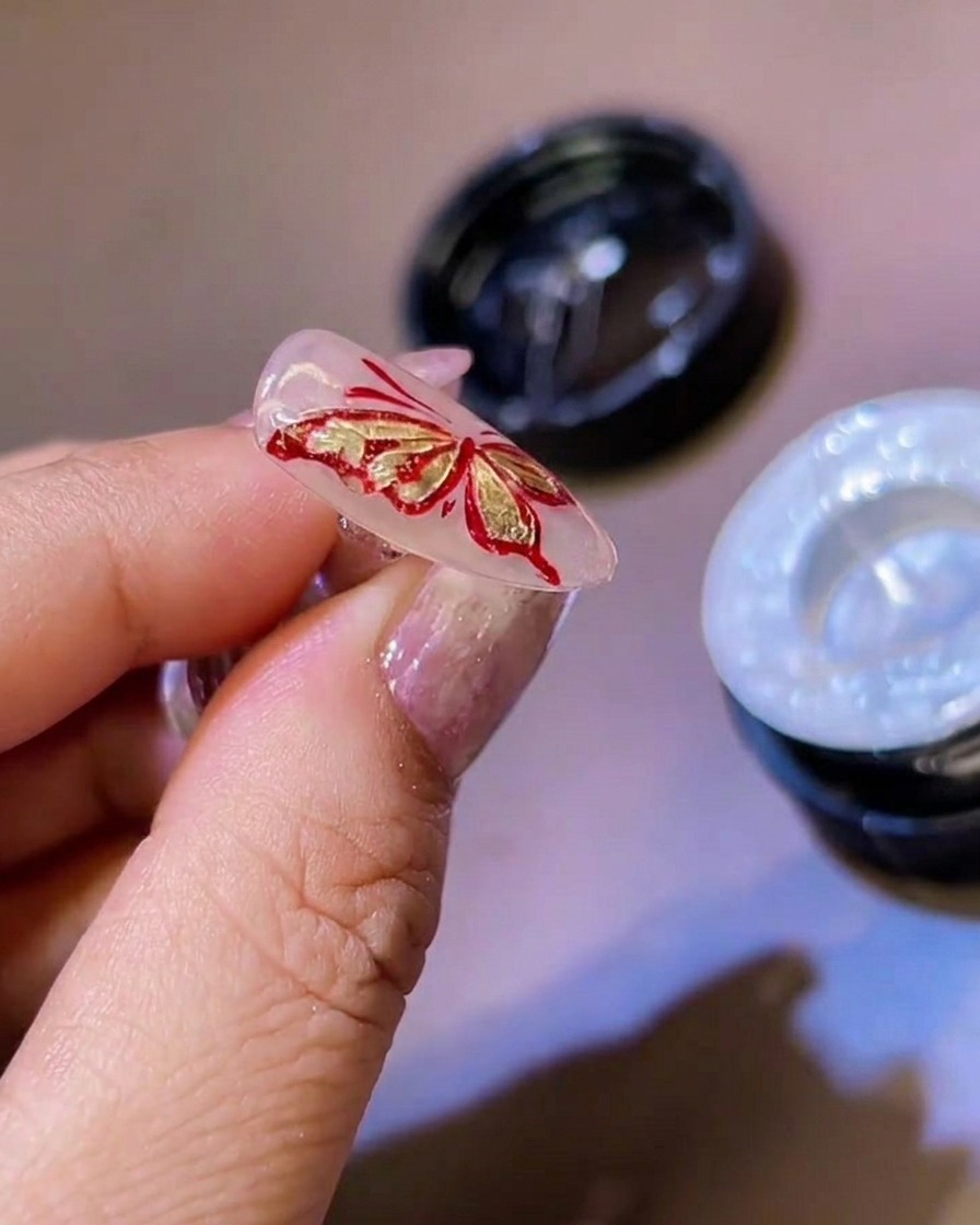 A fine liner brush adding thin white gel details to the edges of 3D butterfly wings.
