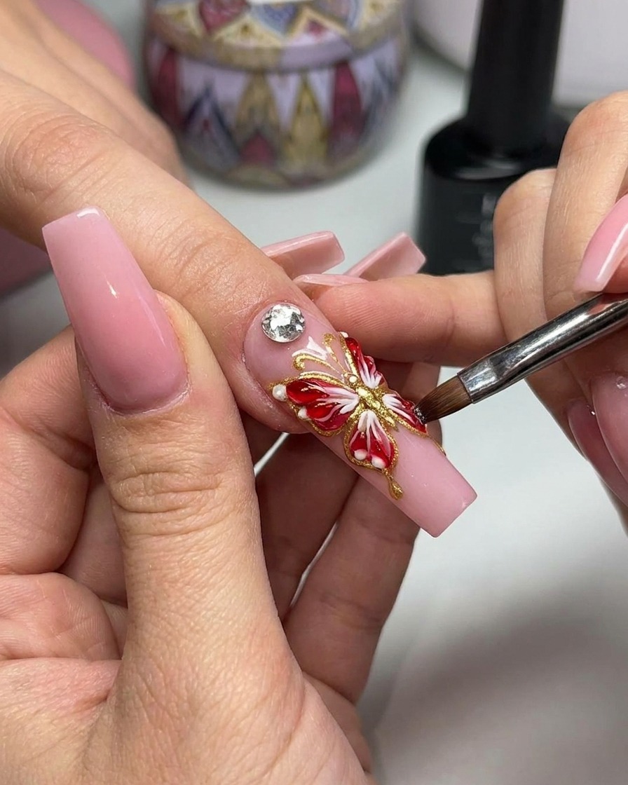 Tweezers placing a sparkling crystal embellishment at the center of a 3D butterfly nail design.