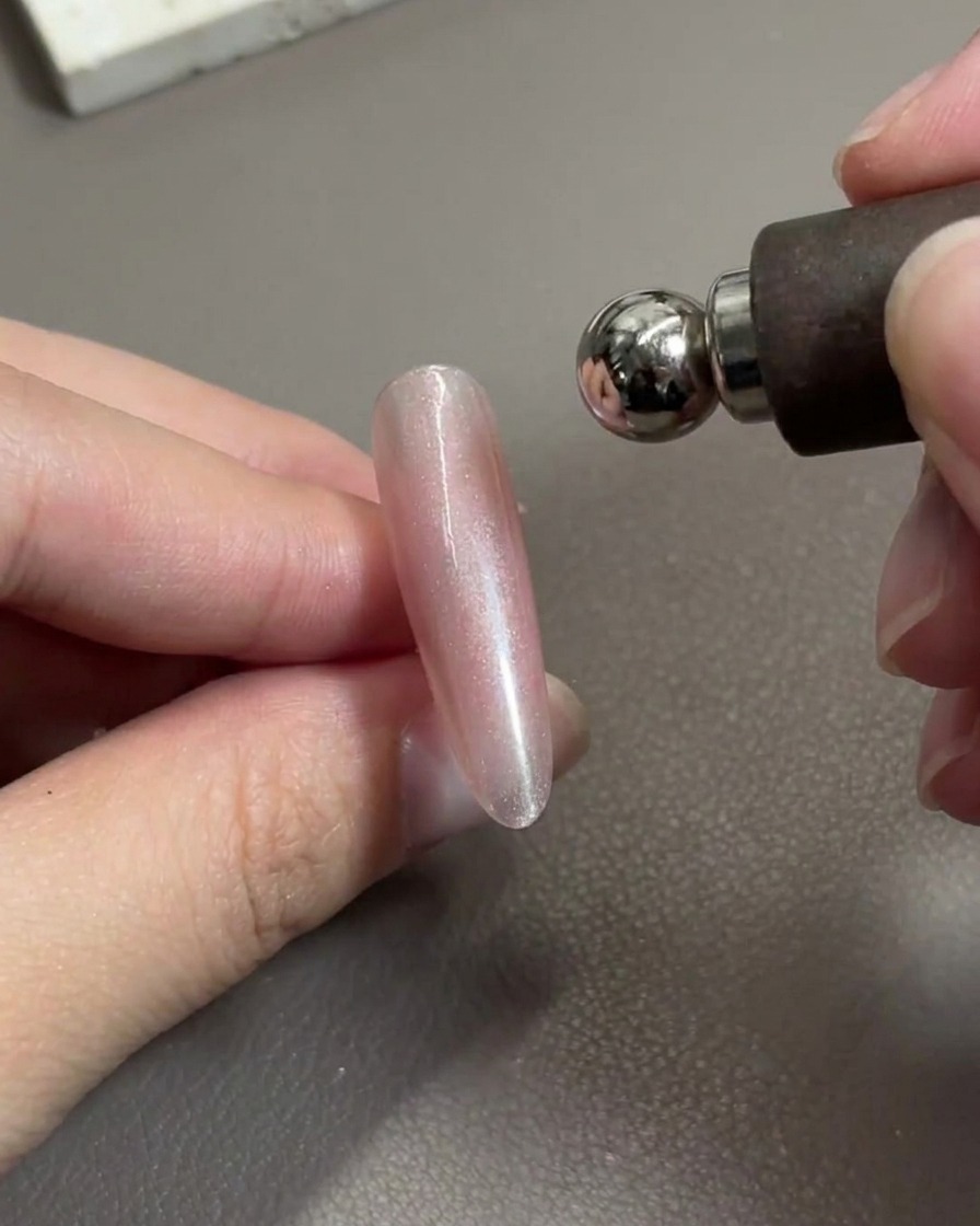 A magnetic nail tool positioned over a glossy pink gel nail, actively shifting the metallic particles.