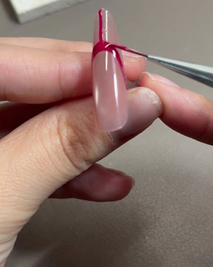 A nail art brush applying rose red gel to fill the space within the French tip outline.