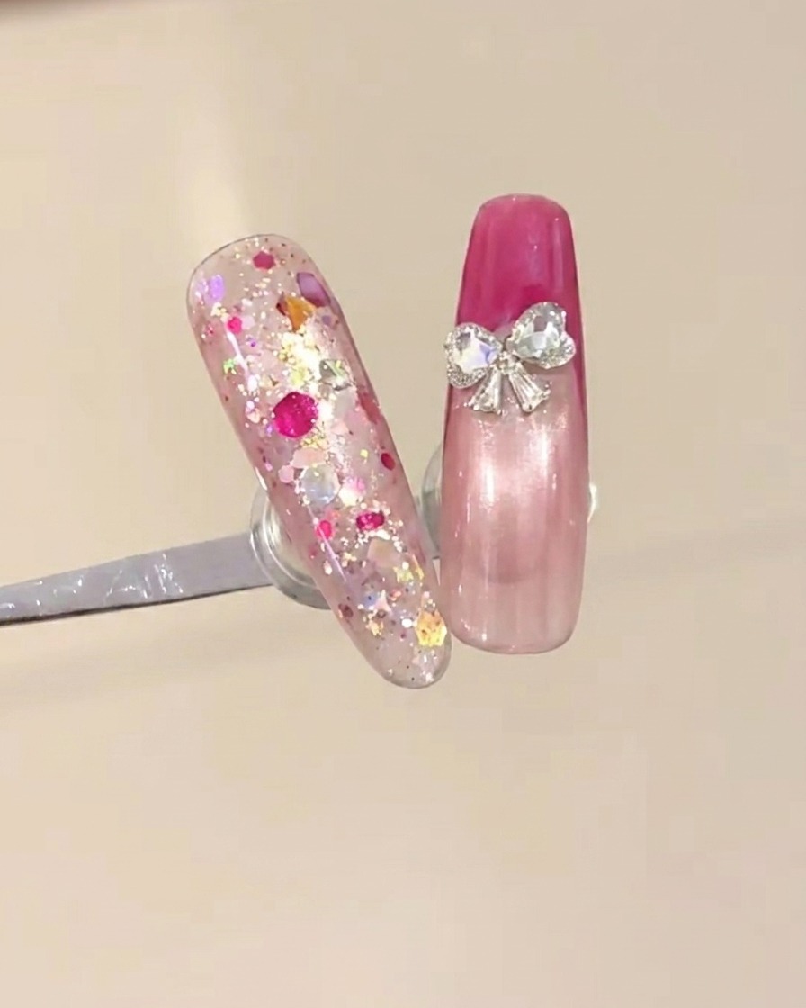 Two small heart rhinestones being placed at the base of the French tip to create a bow design.