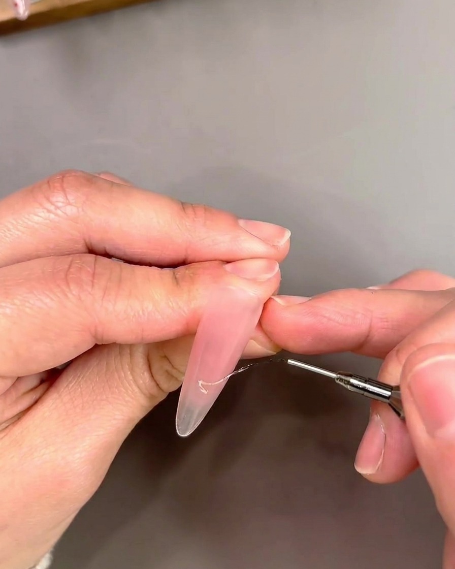 A detail shot of a liner brush applying gold cat-eye gel in a French tip design.