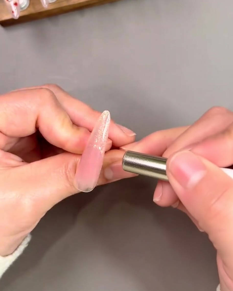 A magnet being held near a gold French tip to create a concentrated, reflective cat-eye effect.