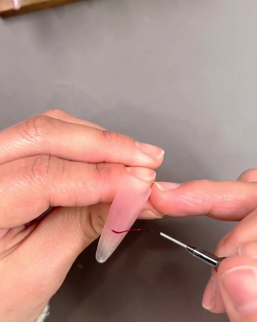 A detail shot of a liner brush outlining a French tip with a fine line of red gel polish.