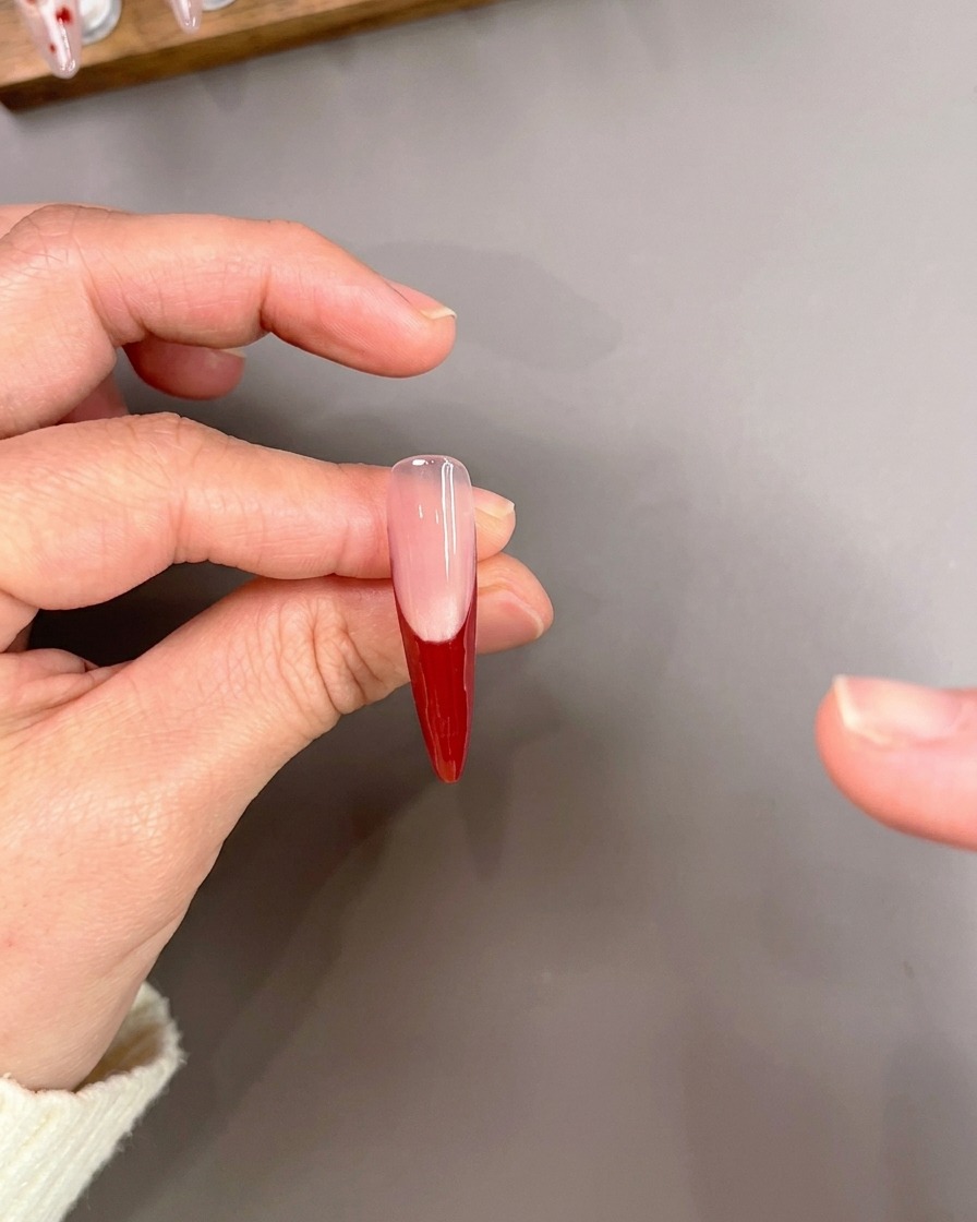 A liner brush carefully drawing thin red lines on a nail tip with a red French manicure base.