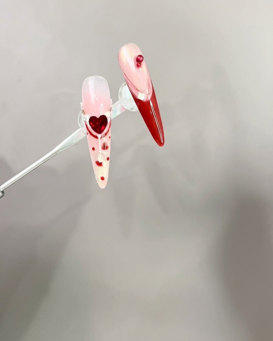 Tweezers placing a red 3D bow charm onto a manicured nail tip.