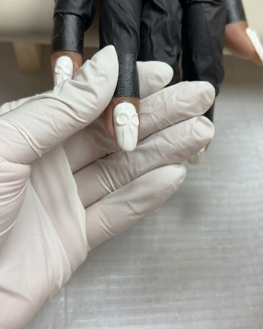 A top-down view of a completed 3D gel bow design on a white nail, held steadily before the final cure.