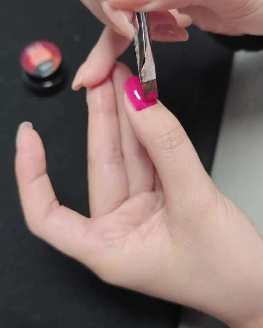 A brush applying a second coat of magenta gel polish over the previously cured layer.