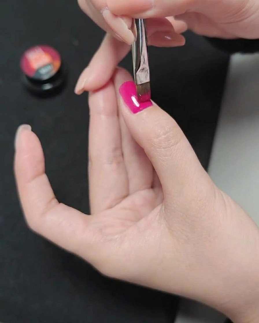 A brush applying a third layer of magenta gel polish, creating a smooth and saturated color finish.