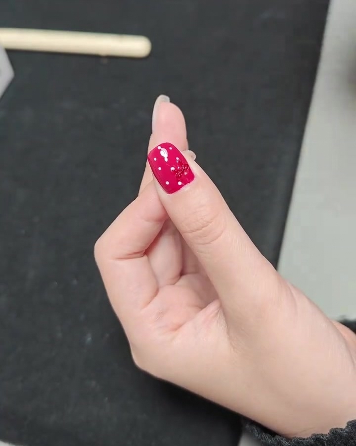 A close-up of a hand with a finished red polka dot bow nail inside a professional UV nail lamp.