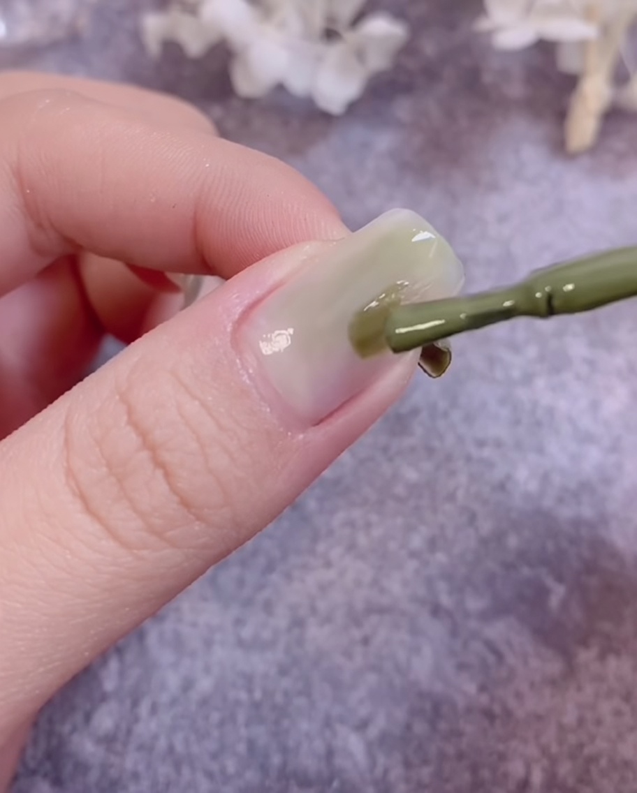 A brush blending green gel polish on a nail surface to create a gradient effect.