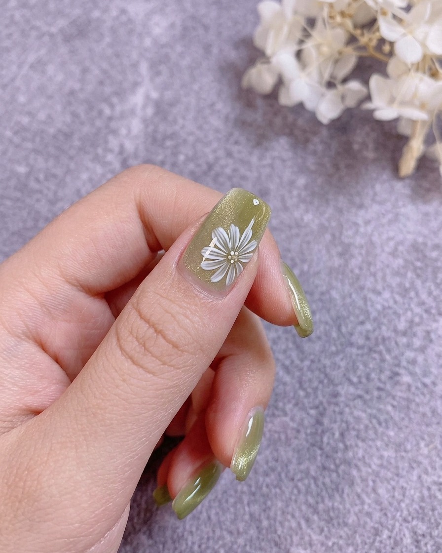 A nail brush applying a clear, hard top coat over a painted floral nail design.