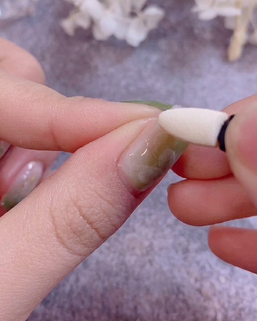 A silicone eyeshadow applicator being used to buff metallic chrome powder onto a gel-painted nail.