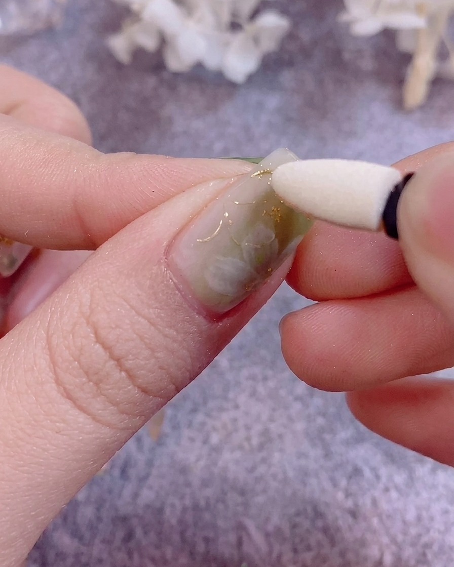 A close-up of tweezers applying delicate flakes of gold leaf onto a painted nail.