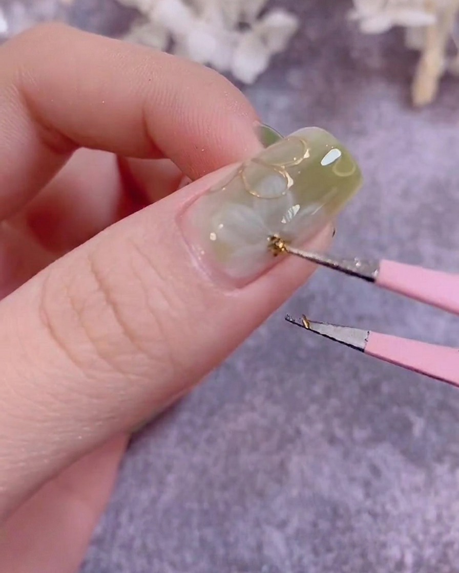 A detail brush painting small green leaves on a manicured nail surface.