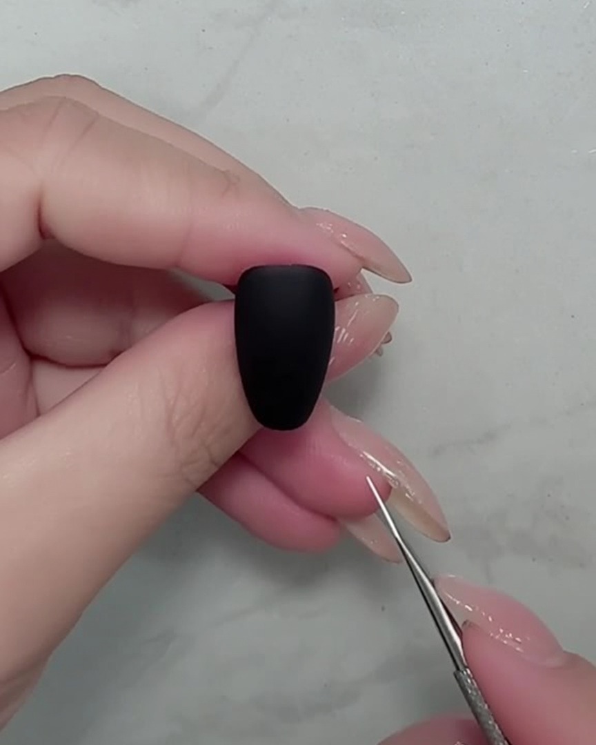 Close-up of a nail brush painting thin white stems on a black matte nail.