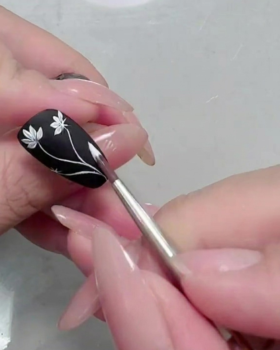 Close-up of a second daisy flower being painted on the black nail.