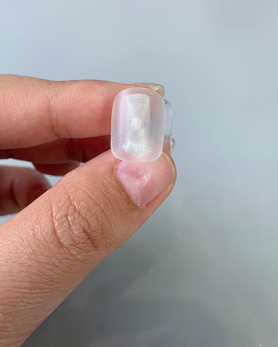 A brush applying a thin layer of light-colored cat-eye gel onto a nail tip.