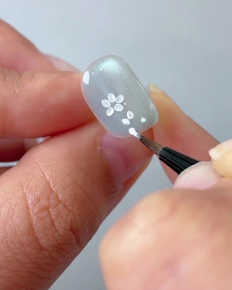 A liner brush adding more white petal details to a floral cluster on the nail.