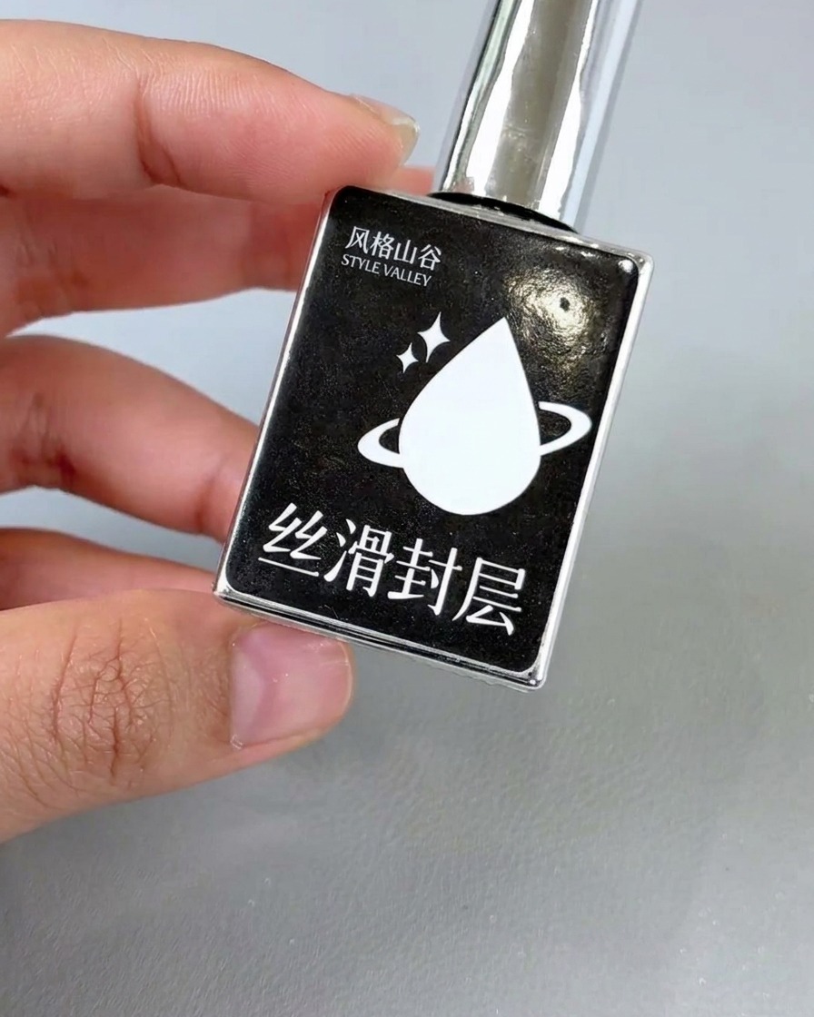 A nail polish brush applying clear glossy top coat to a finished floral nail design.