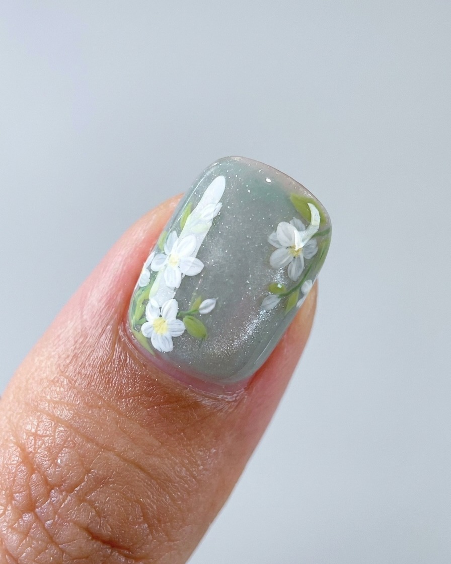 A close-up of a brush adding white detail to daisy petals on a nail.