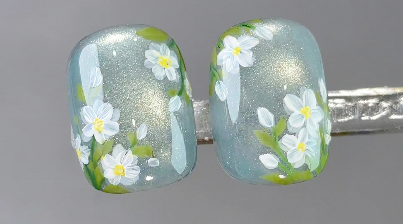 A detailed close-up of clear cat-eye gel nails adorned with hand-painted white daisies and soft green foliage.