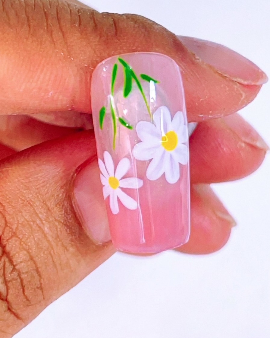 A view of the nail design showing the second daisy with a bright yellow center dot, ready for final curing.