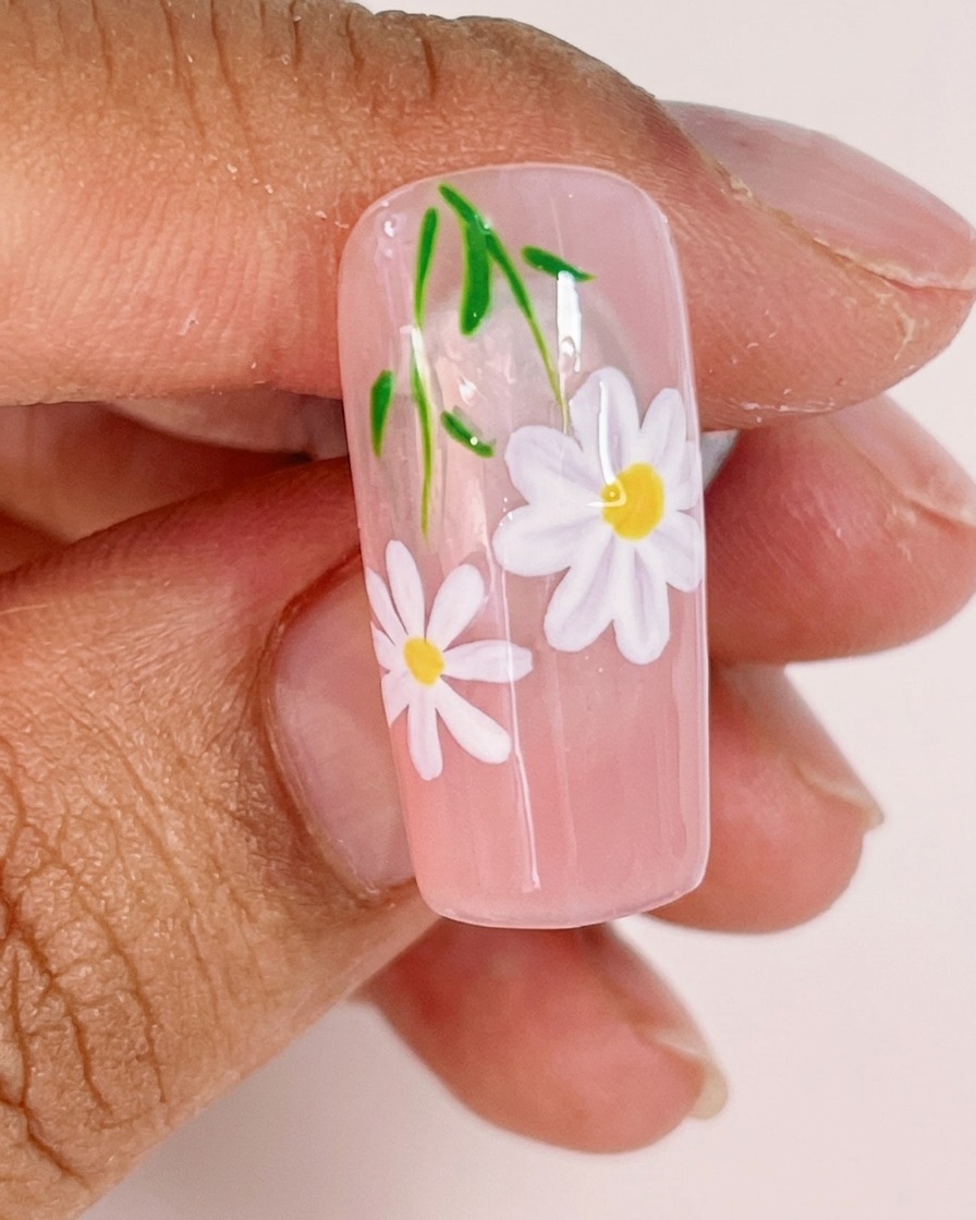 A close-up showing a fine liner brush adding thin green stems and small leaves to the daisy nail art design.