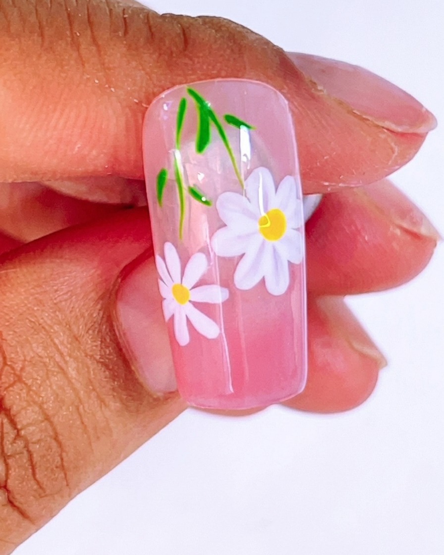 A brush applying a thick, glossy layer of clear top coat over the finished daisy and leaf design.
