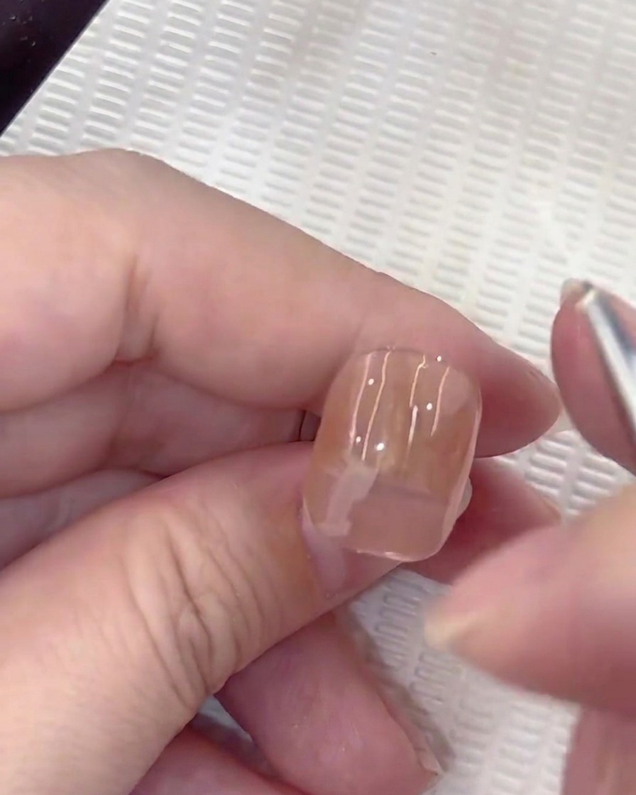 A small round brush performing a press-and-lift motion to create a white petal on the nail.